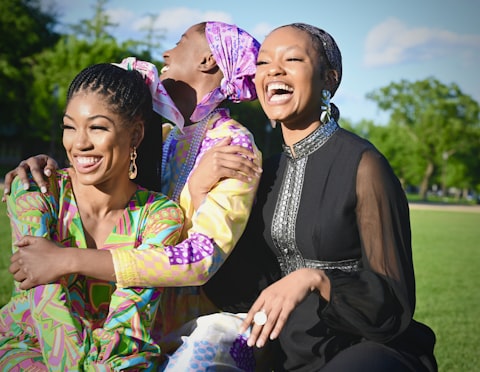 Three women in colorful outfits mid-laugh, arms around each other in a park